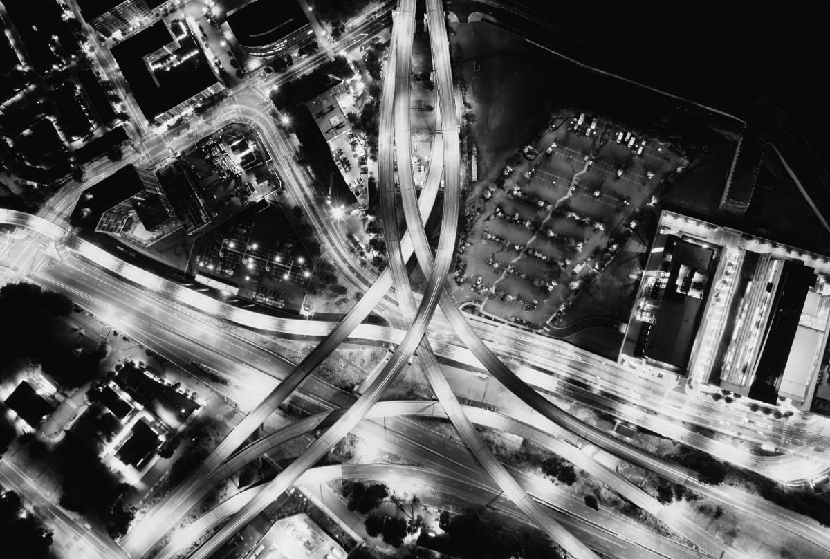An aerial photograph of a network of illuminated highway on- and offramps taken at night.