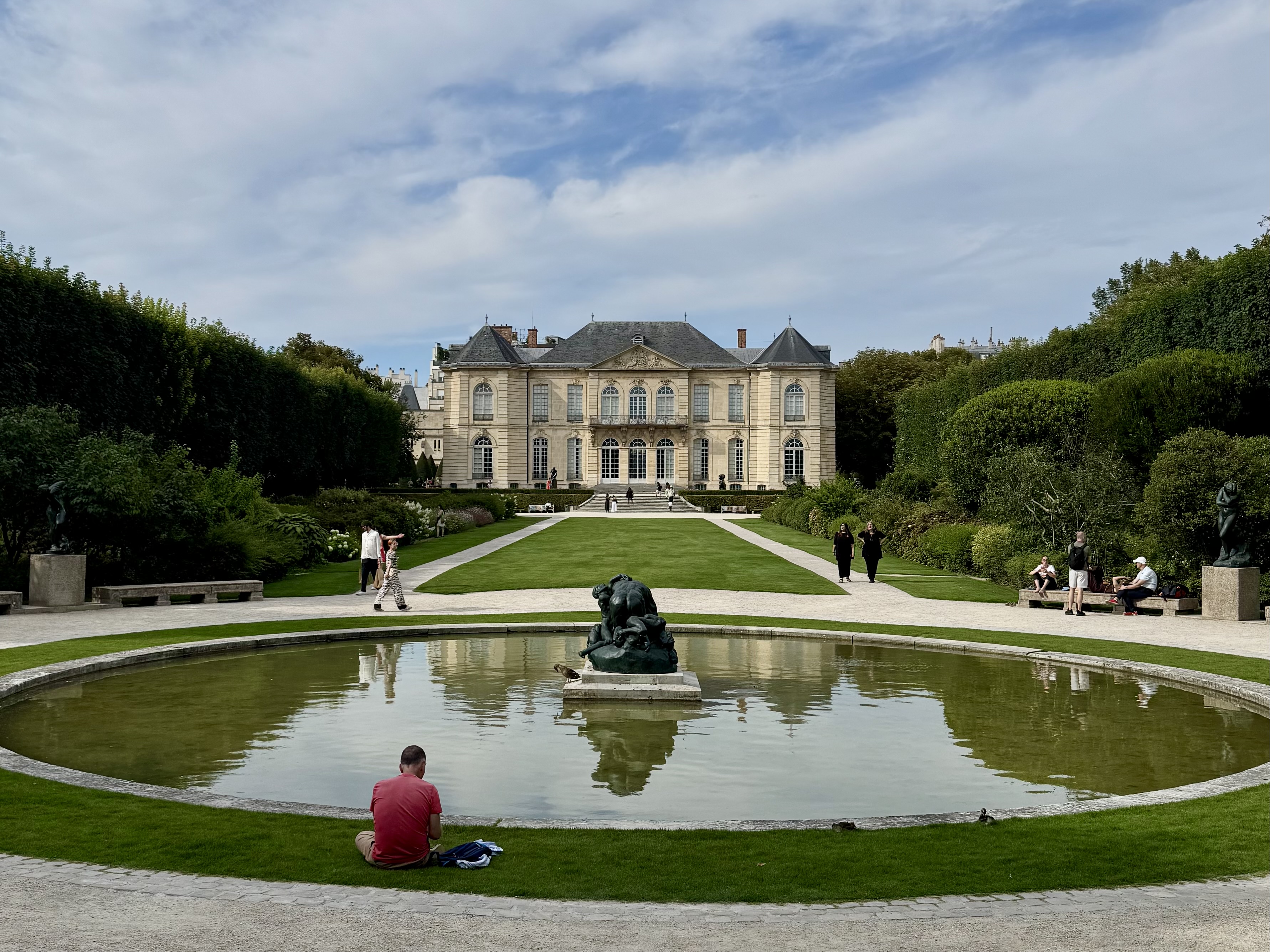 A photograph of a European mansion and its grounds, with a fountain in front that has a bronze sculpture in the middle. Grounds of the Museé Rodin in Paris